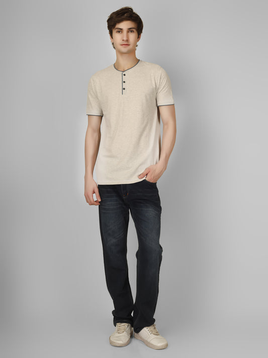 Man wearing a beige henley shirt and dark jeans on a gray background