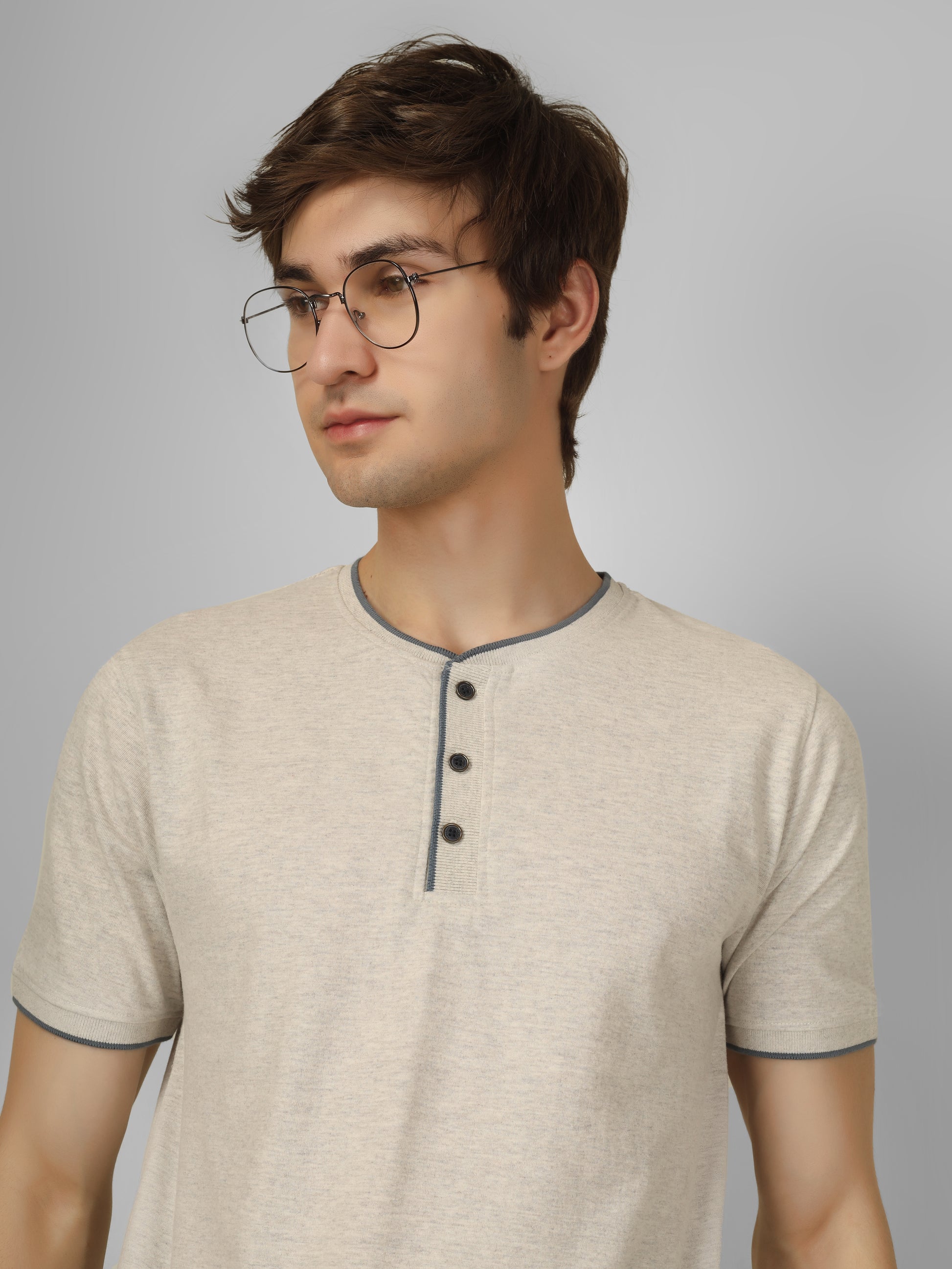 Man wearing a beige henley shirt with black buttons on a gray background